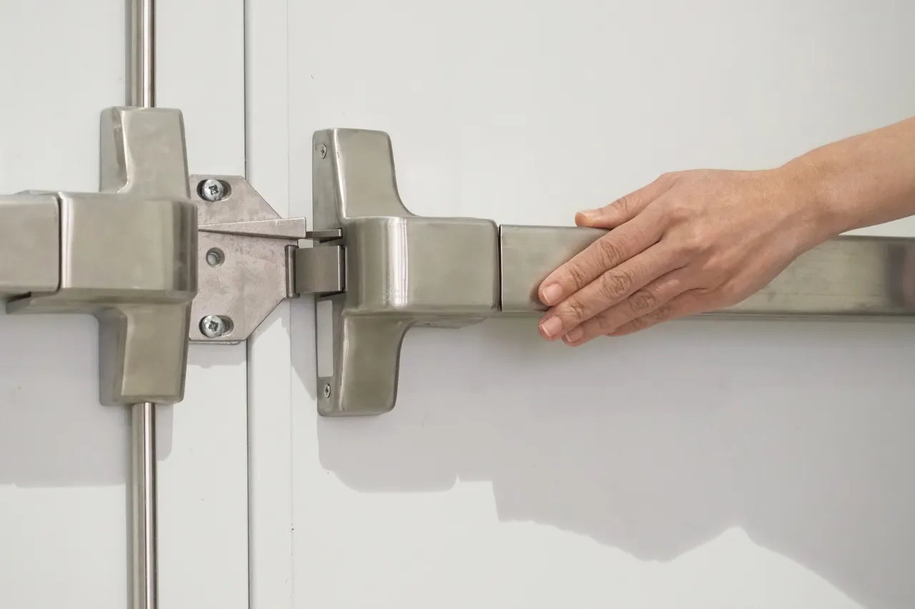 Mano chiude un chiavistello metallico su porta bianca