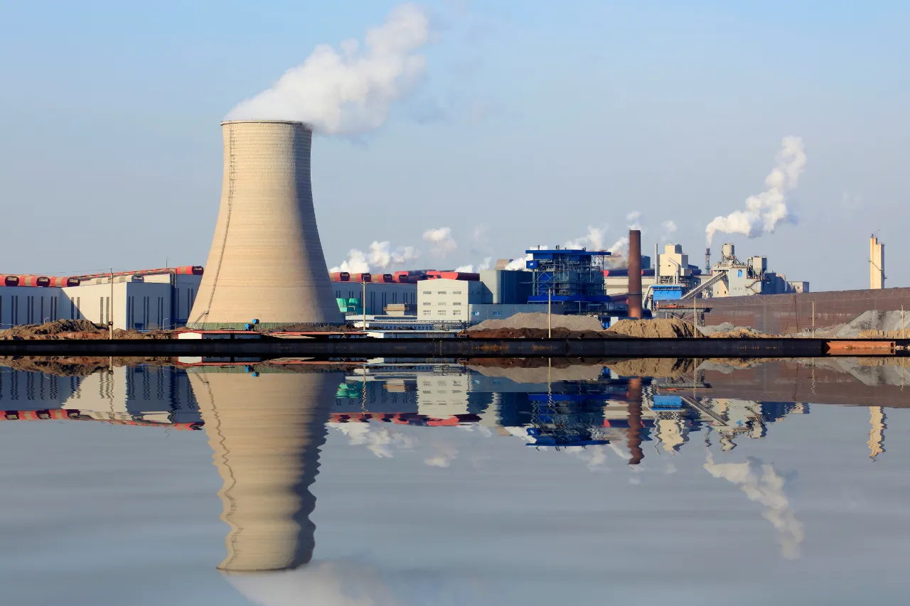 Impianto industriale con torre di raffreddamento riflessa nell’acqua