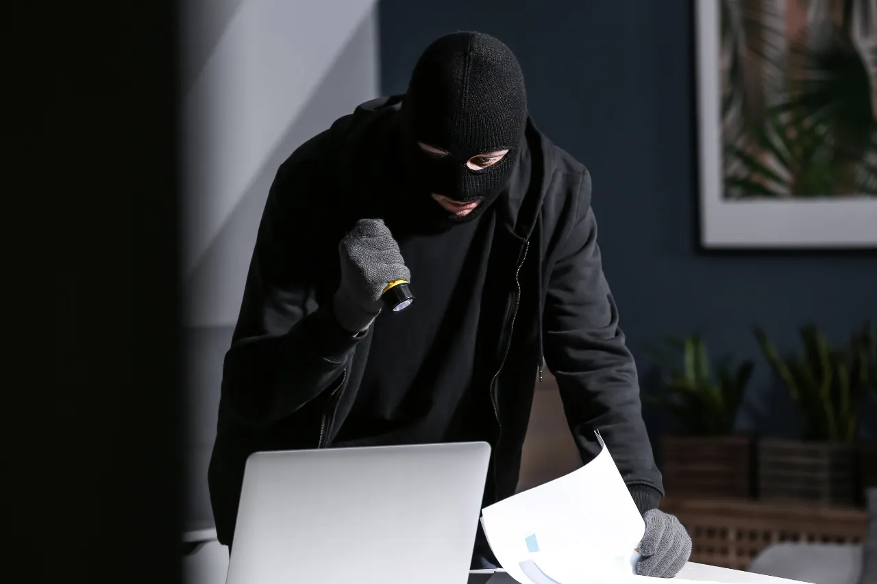 Ladro mascherato con torcia vicino a laptop e documenti