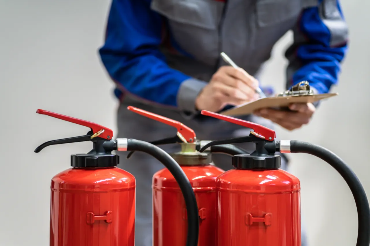 Tecnico ispeziona estintori rossi con checklist