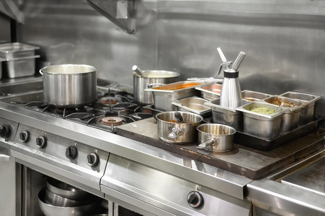 Cucina professionale con fornelli, pentole e vaschette di ingredienti