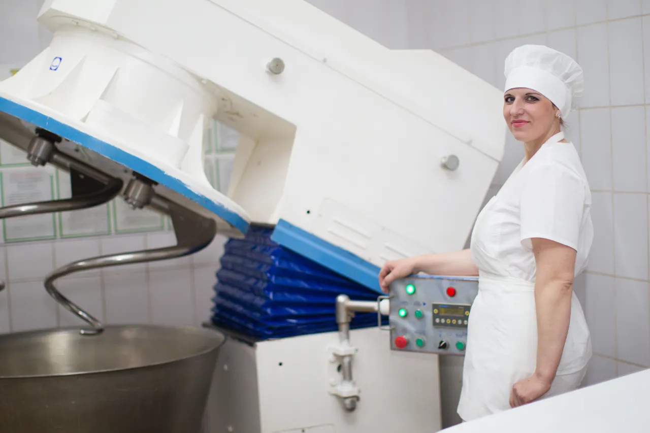 Fornaia accanto a impastatrice industriale in laboratorio