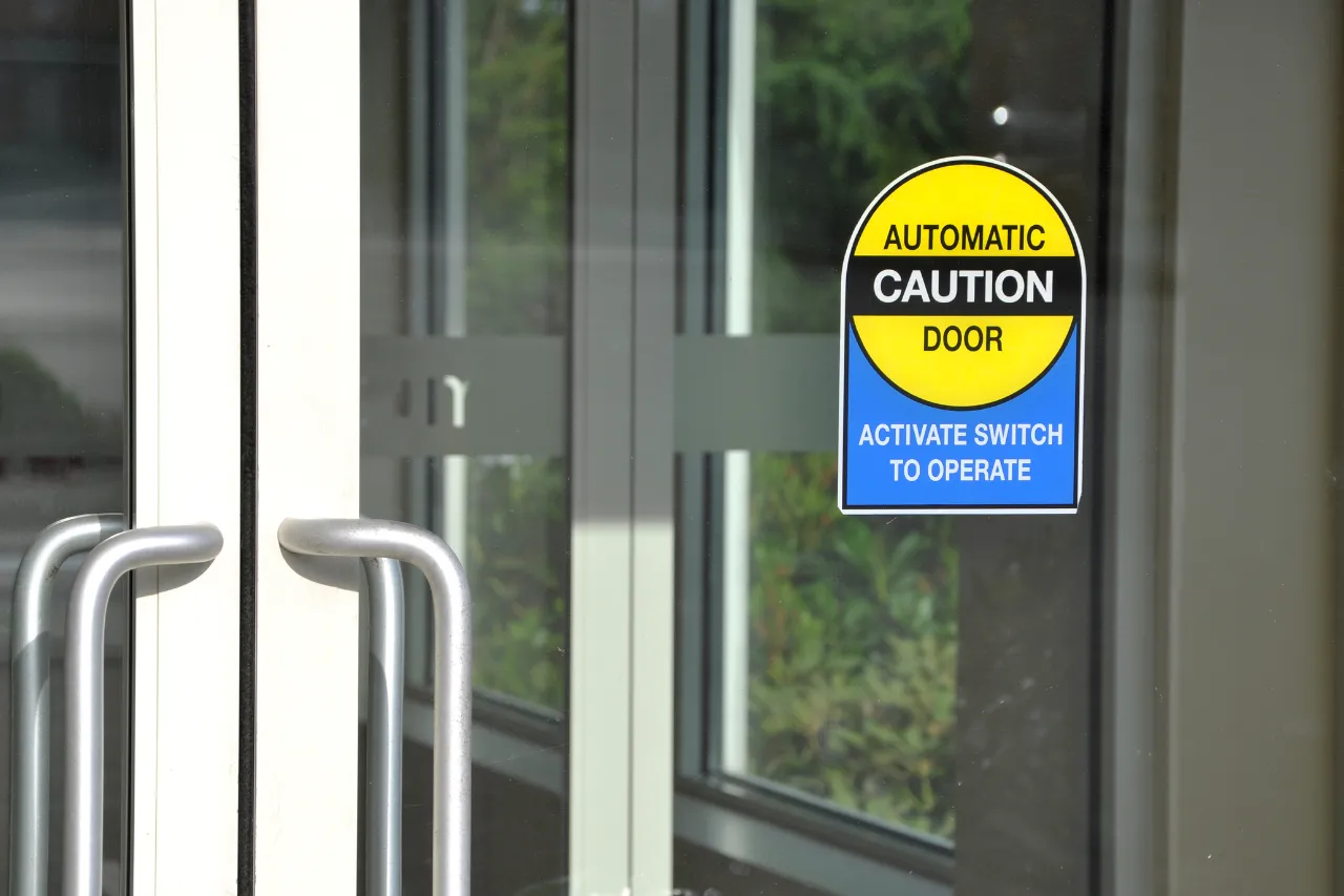 Porta automatica in vetro con cartello di avviso