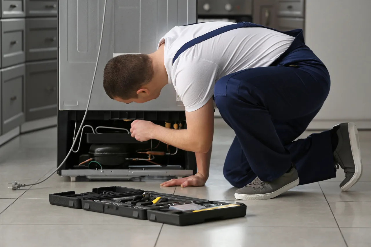 Tecnico ripara il retro di un frigorifero in cucina