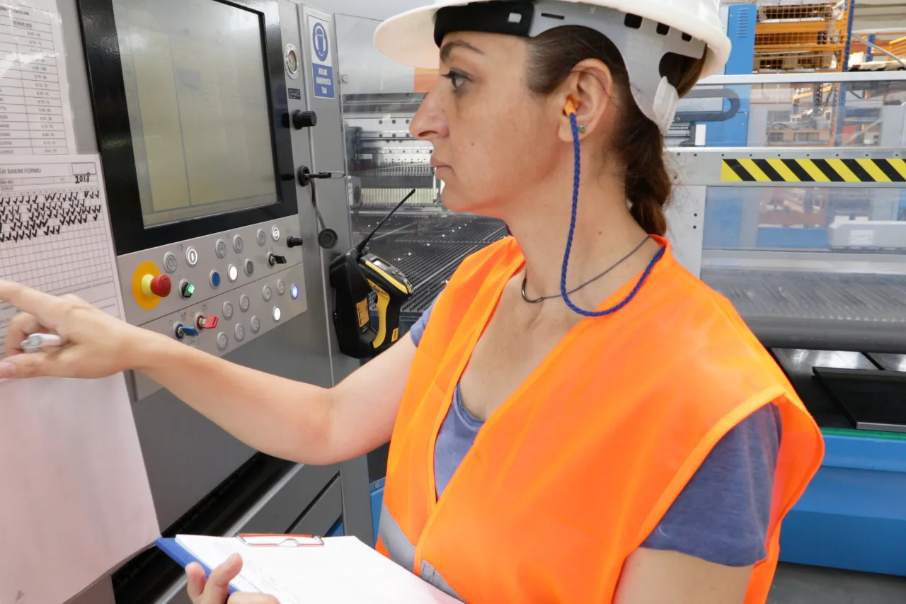 Operaia controlla macchinario industriale con casco e giubbotto alta visibilità