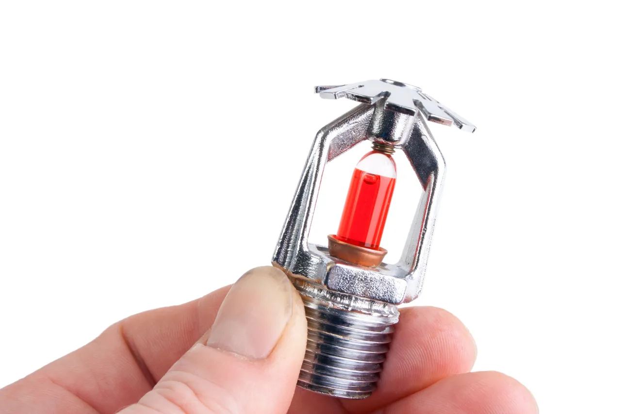 Mano che tiene testina sprinkler antincendio con ampolla rossa