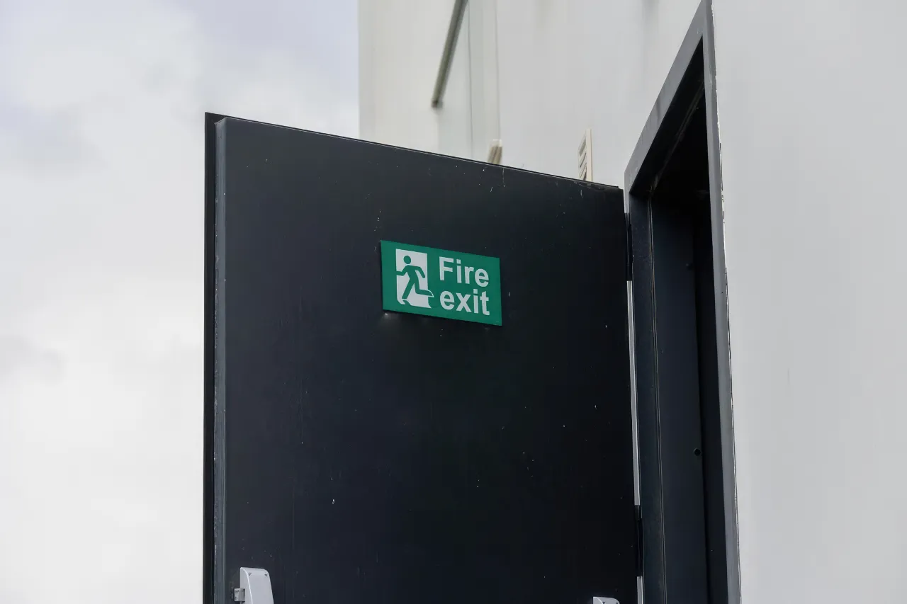 Porta nera aperta con cartello verde uscita antincendio