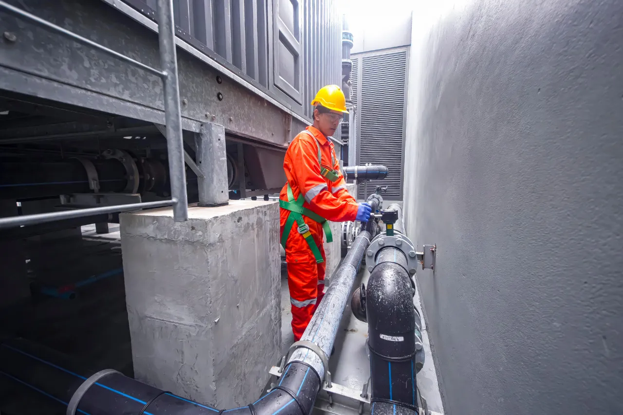 Tecnico controlla tubazioni industriali con casco e tuta arancione