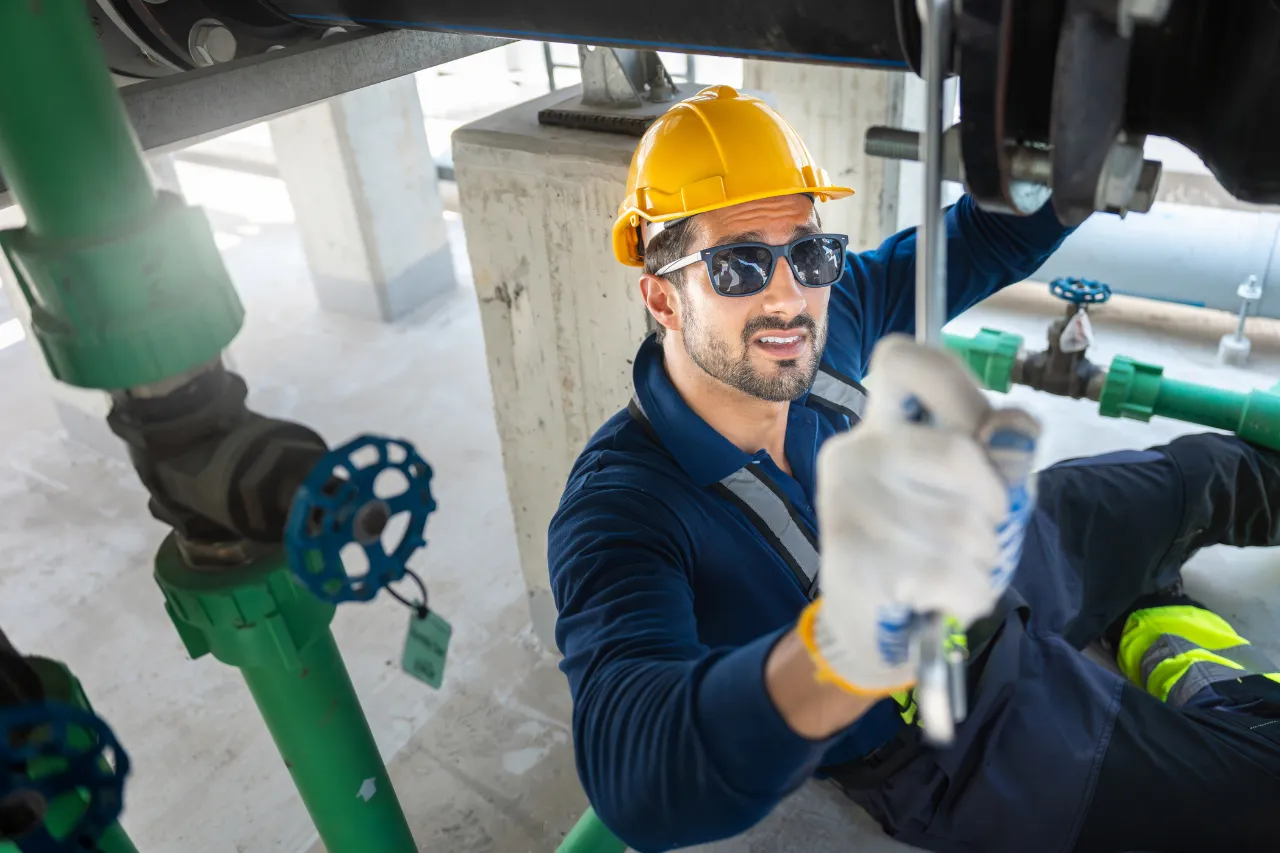 Tecnico controlla tubazioni industriali con casco e occhiali protettivi