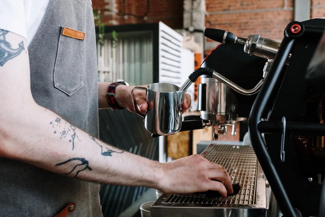 Barista prepara latte montato con macchina espresso professionale