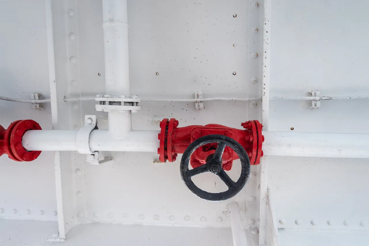 Valvola rossa con volantino su tubazione bianca industriale