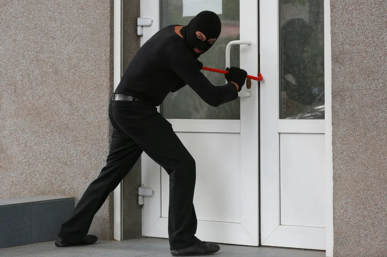 Ladro mascherato forza una porta con un piede di porco